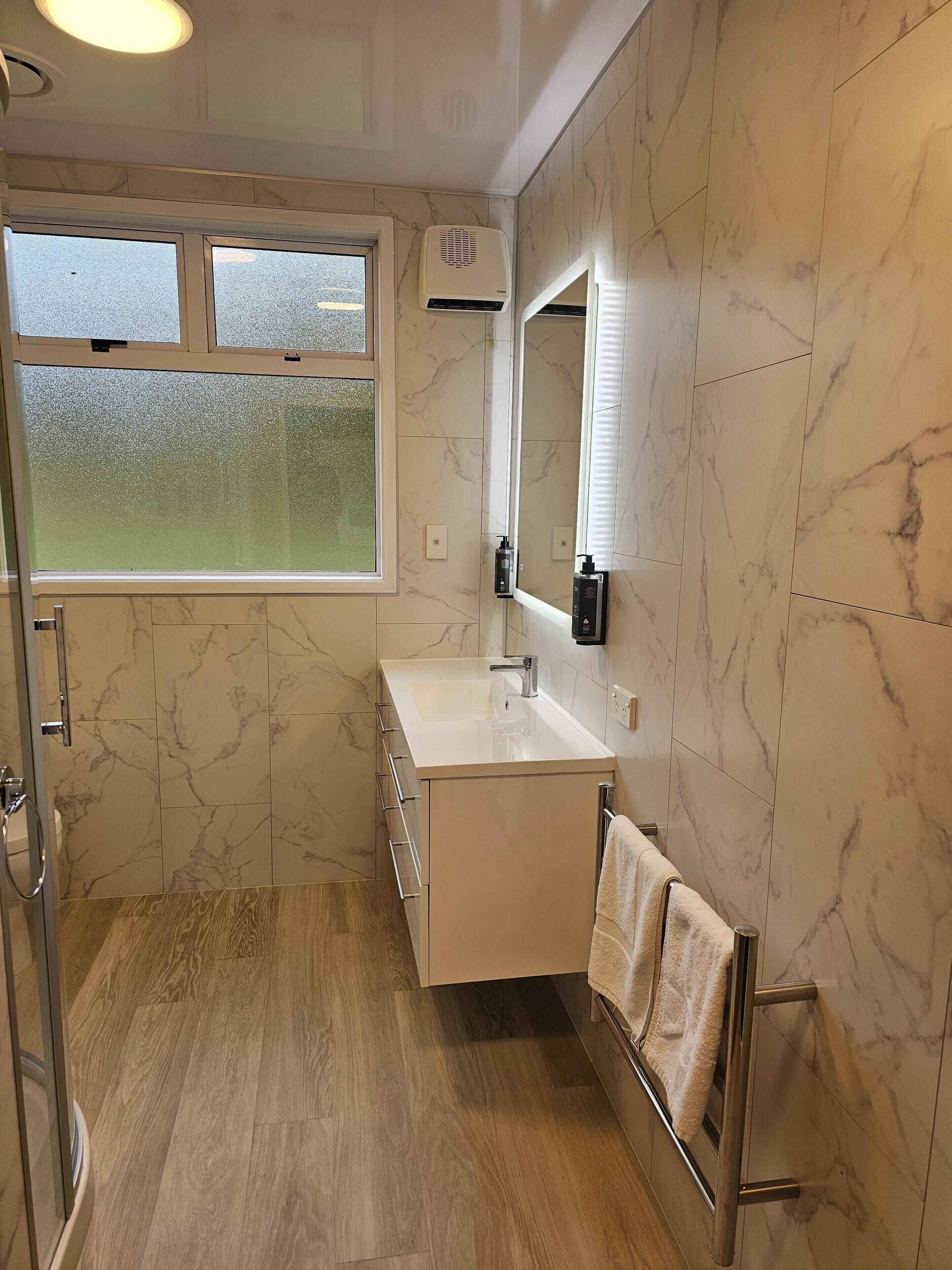 A modern bathroom with a glass shower enclosure, a vanity with a sink, and a towel rack.