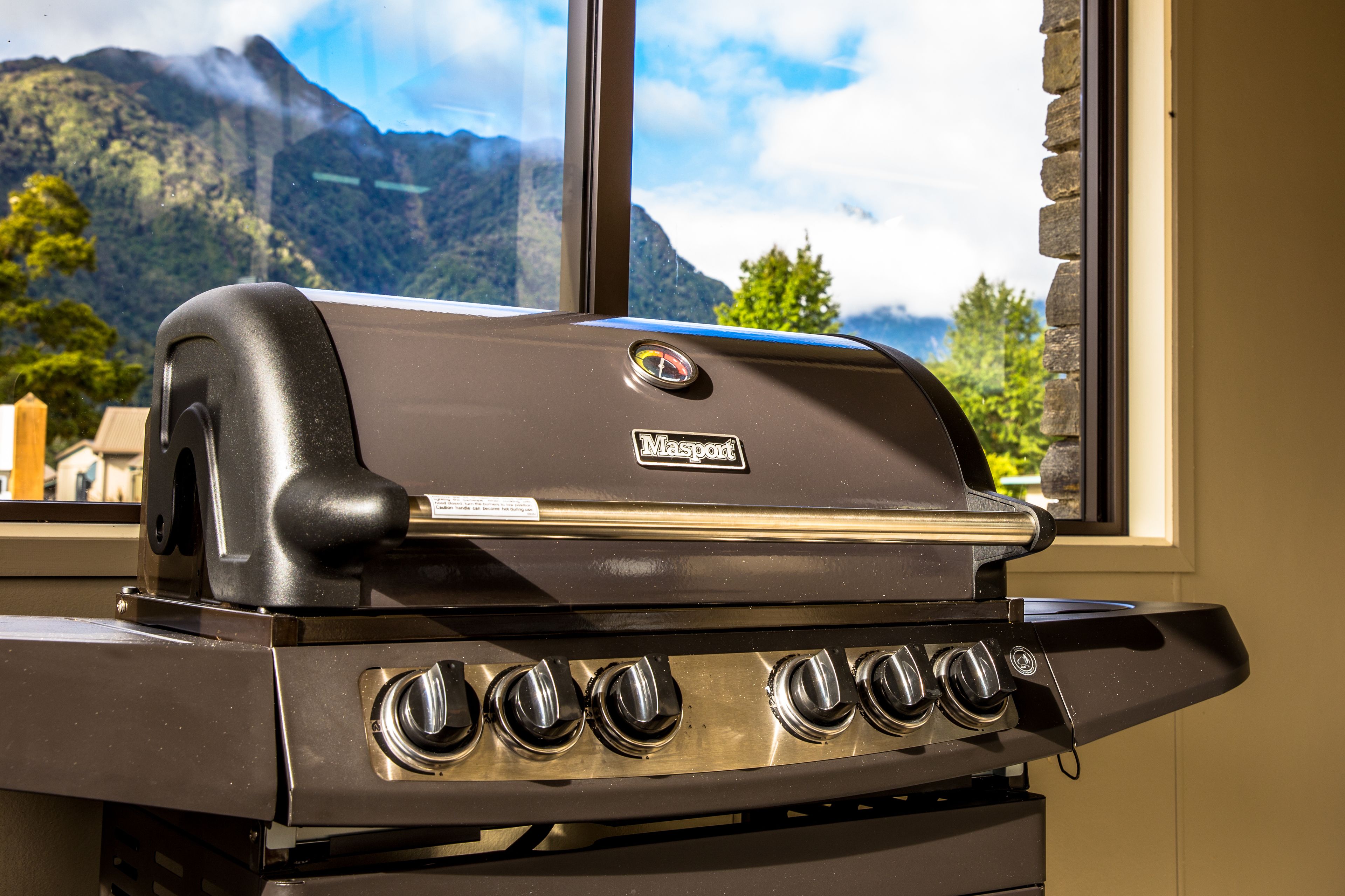 Una parrilla de gas Weber con cuatro quemadores, ubicada frente a una ventana con vistas a la montaña.