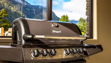 Una parrilla de gas Weber con cuatro quemadores, ubicada frente a una ventana con vistas a la montaña.
