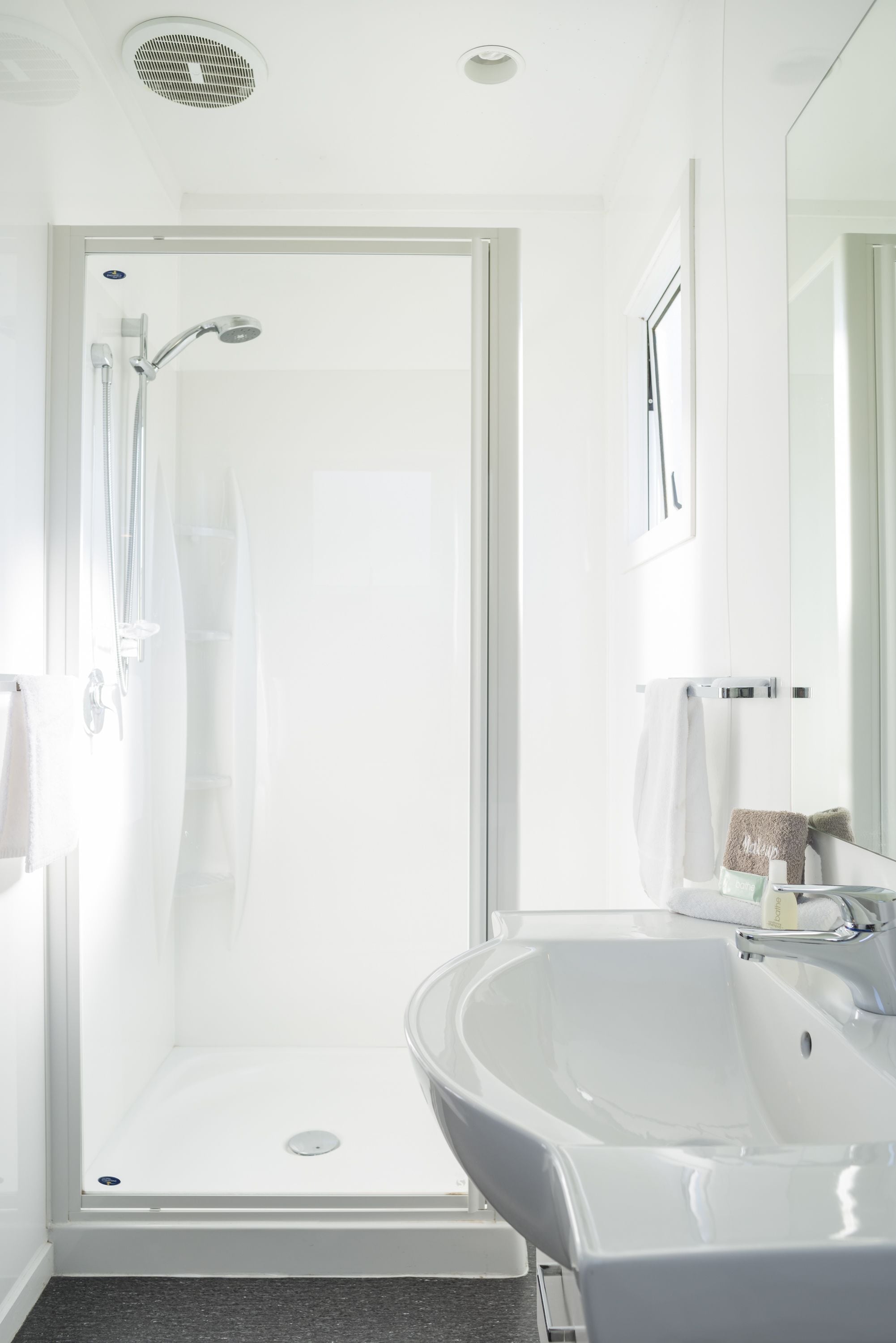 Ein modernes Badezimmer mit einer gläsernen Dusche, einem weißen Waschbecken und einem großen Spiegel.