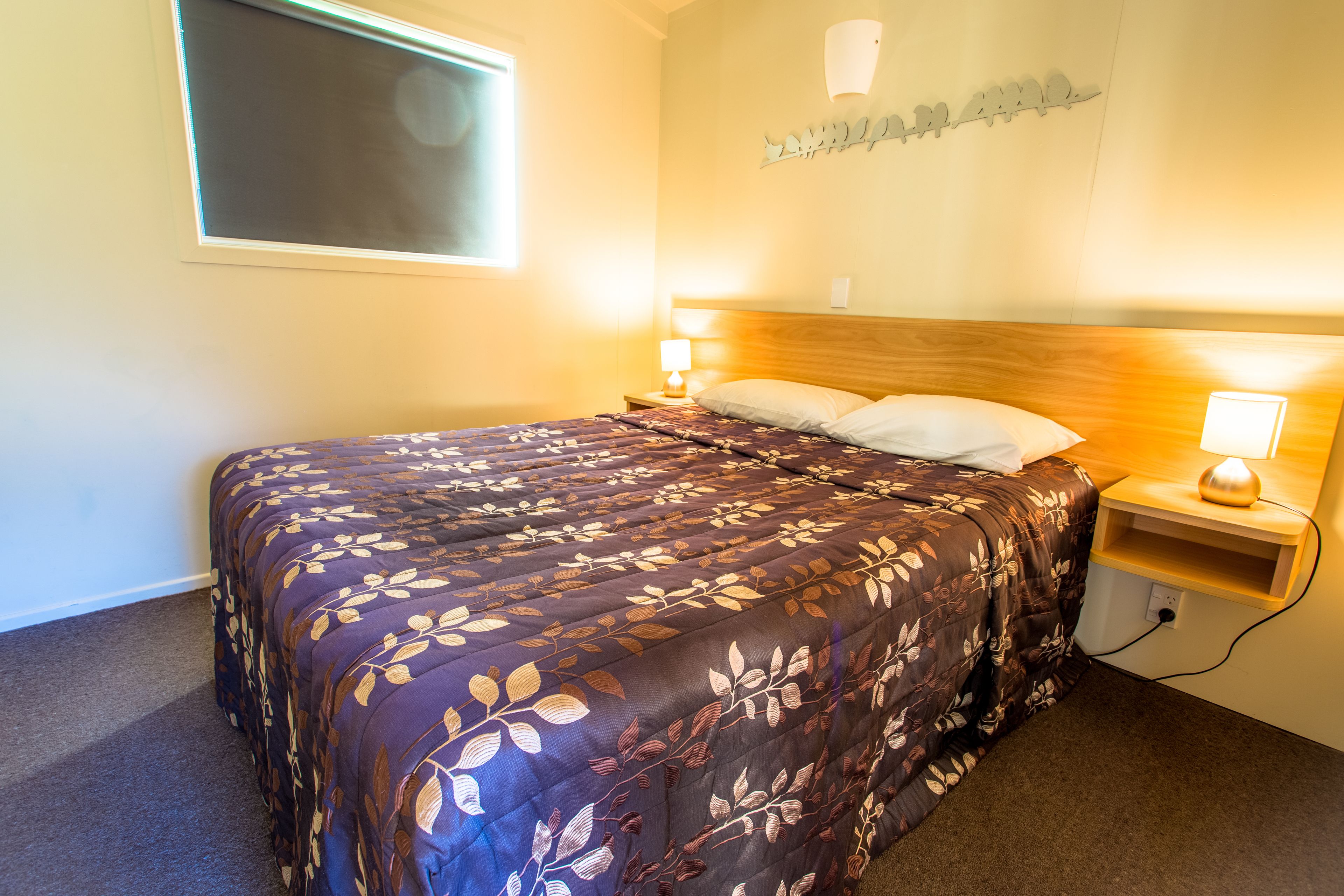 A neatly made bed with a floral bedspread, two bedside lamps, and a wall-mounted light fixture.