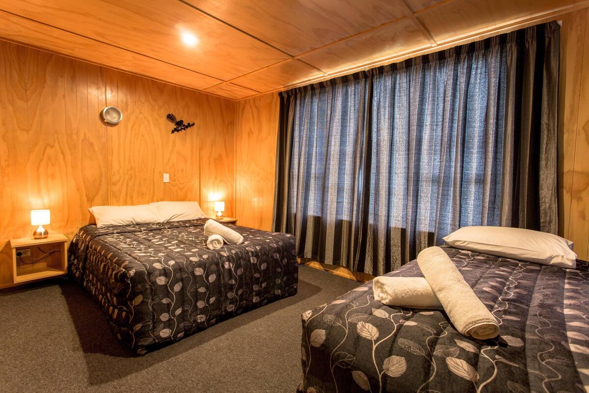 Habitació d'hotel amb dos llits, parets de fusta, una finestra gran amb cortines i làmpades de nit.