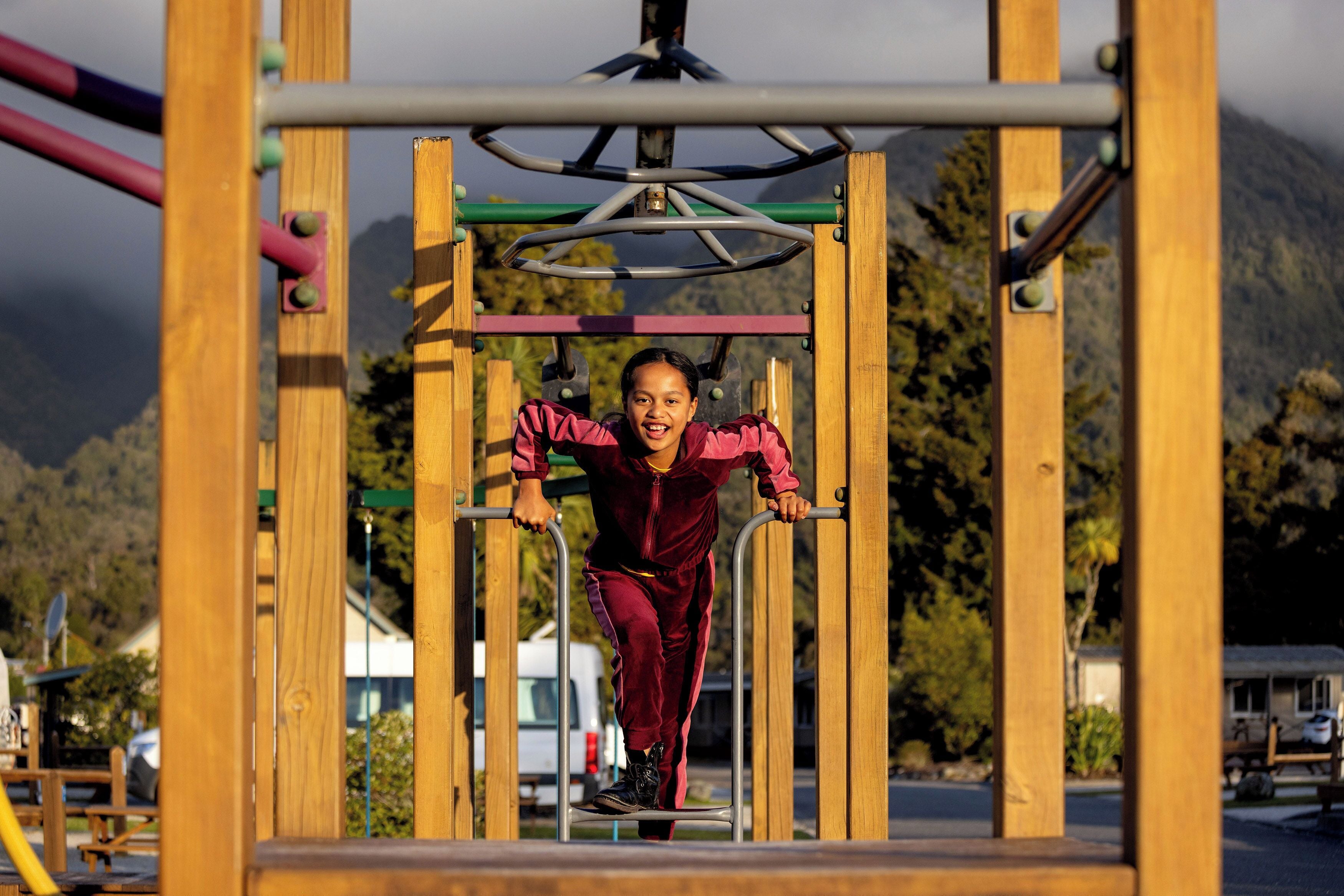 A person using a playground structure with a metal frame and wooden beams.