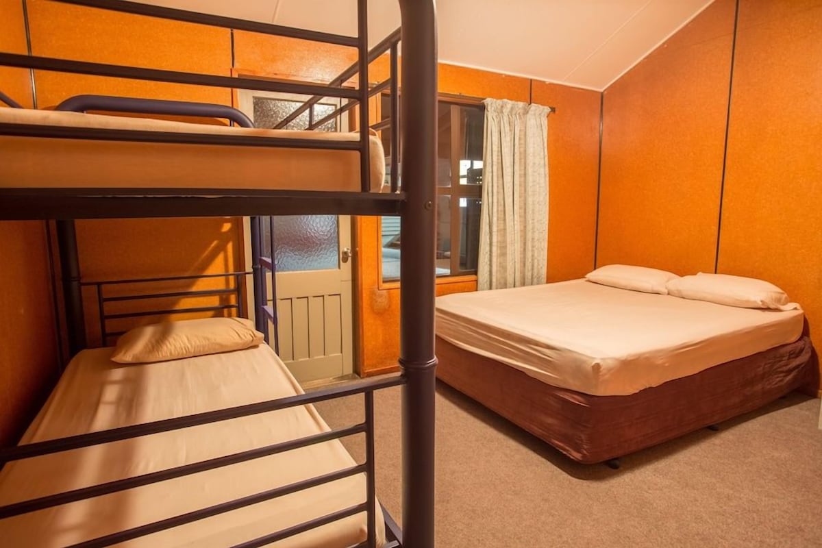 Une chambre avec des lits superposés, un lit simple, une fenêtre avec des rideaux et une porte.