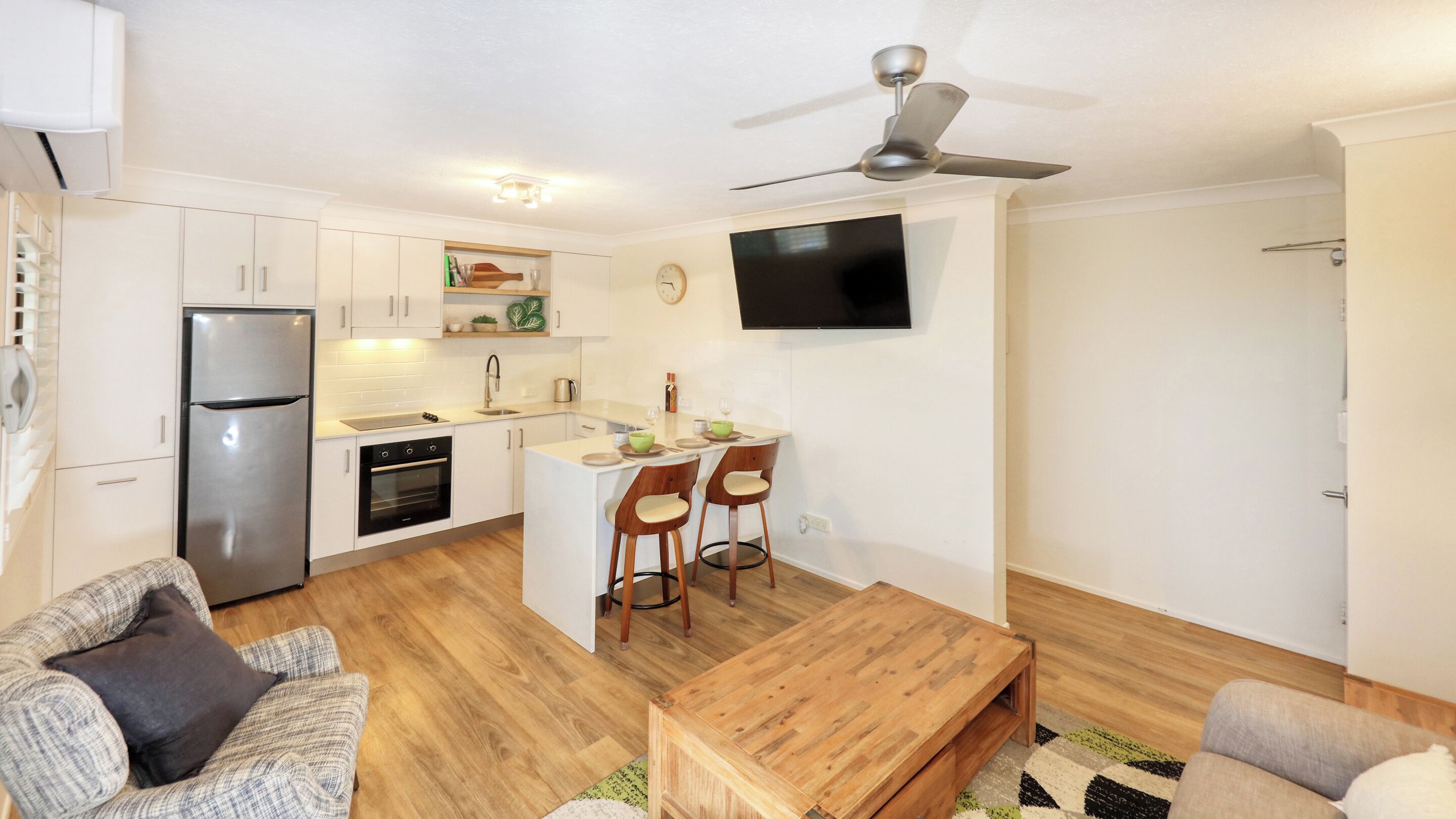 A compact apartment with a kitchenette, a dining area, a living room with a sofa, and a TV mounted on the wall.