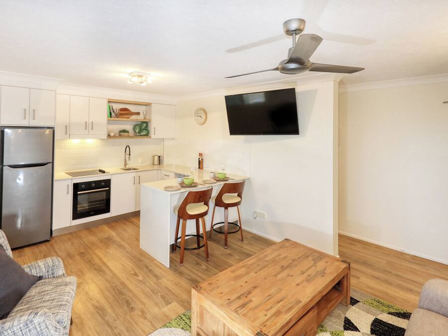 Un appartement compact comprenant une kitchenette, un coin repas, un salon avec un canapé et un téléviseur fixé au mur.