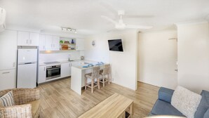 Una cocina moderna con armarios blancos, horno empotrado y comedor con sillas de mimbre.