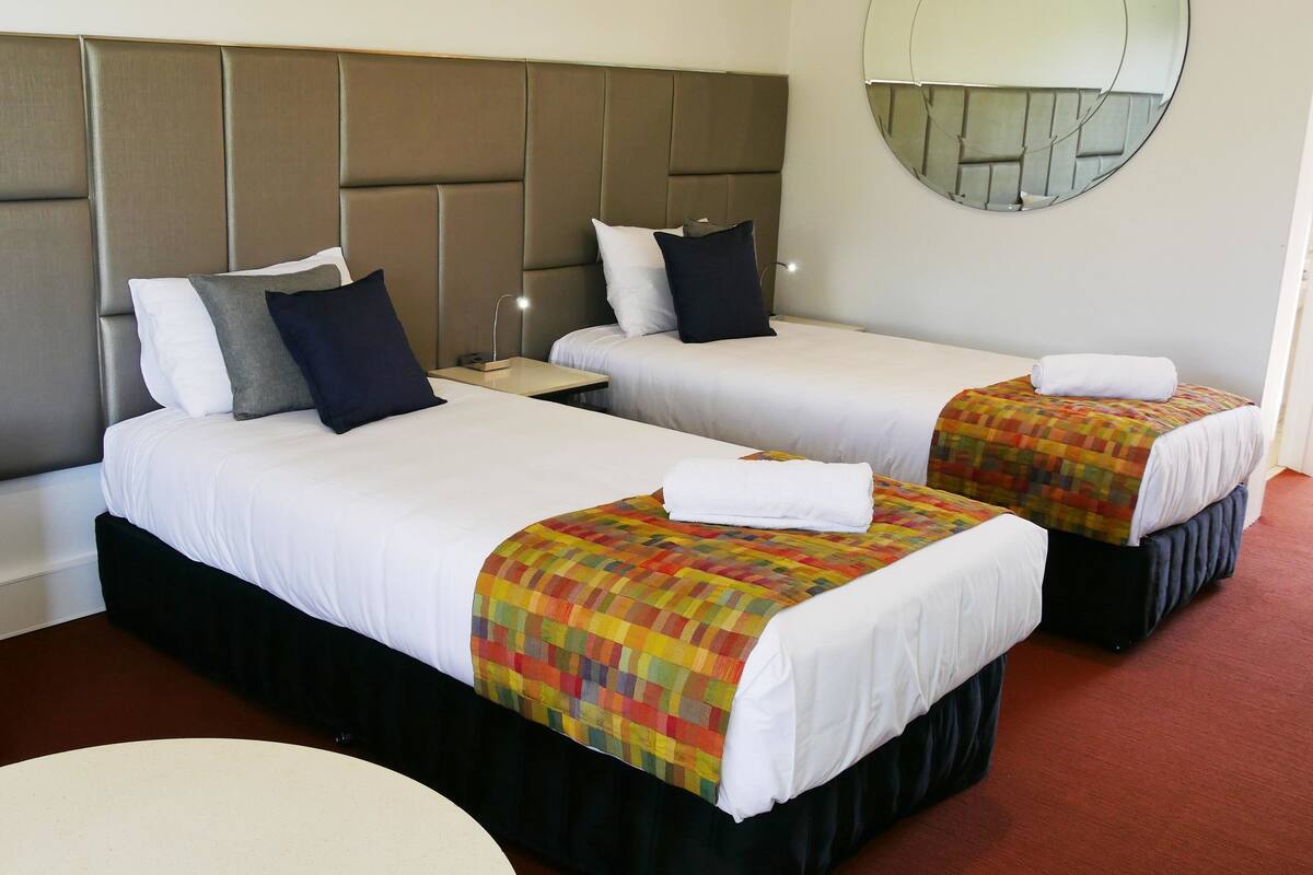 A hotel room with two beds, a sofa, a round table, and a large mirror on the wall.