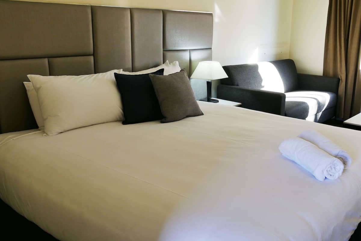 A hotel room with a large bed, a bedside table, a chair, and a lamp.
