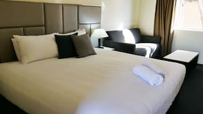 A hotel room with a large bed, a bedside table, a chair, and a lamp. - Country Capital Motel (South Tamworth)