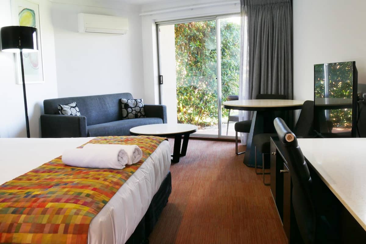 A hotel room with a bed, a sofa, a dining table, and a desk.