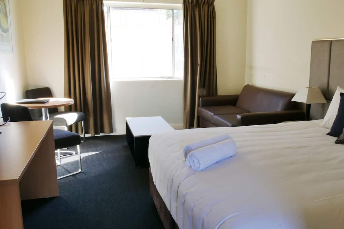 A hotel room with a bed, a desk, a chair, a sofa, and a window with curtains.