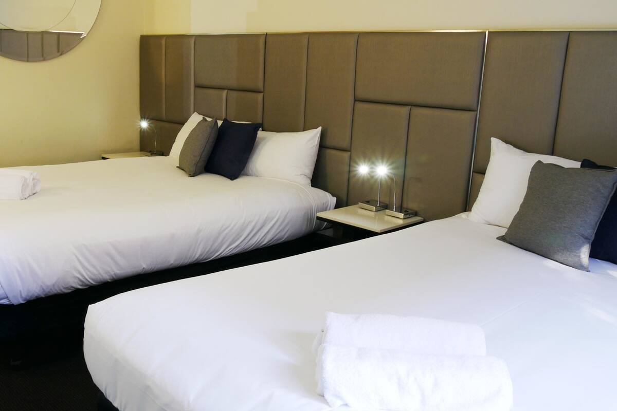 Two single beds with white linens and pillows, a bedside table with a lamp, and a round mirror on the wall.