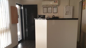 A modern kitchen with a central island, a refrigerator, and a microwave. There is a window with blinds and a door leading to another room. - Country Capital Motel (South Tamworth)