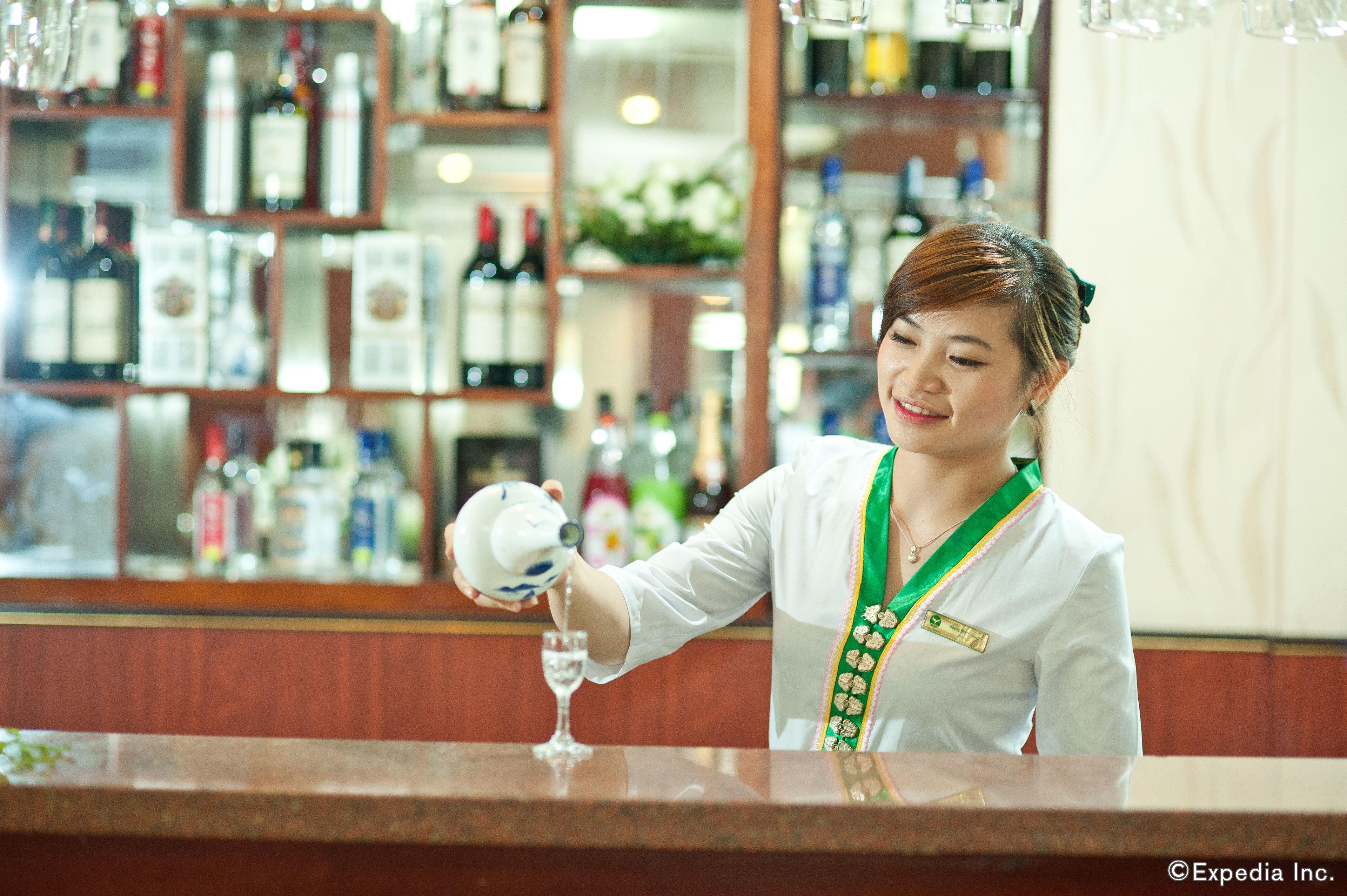 Una persona serviendo té en un vaso en un bar, con estantes llenos de botellas al fondo.