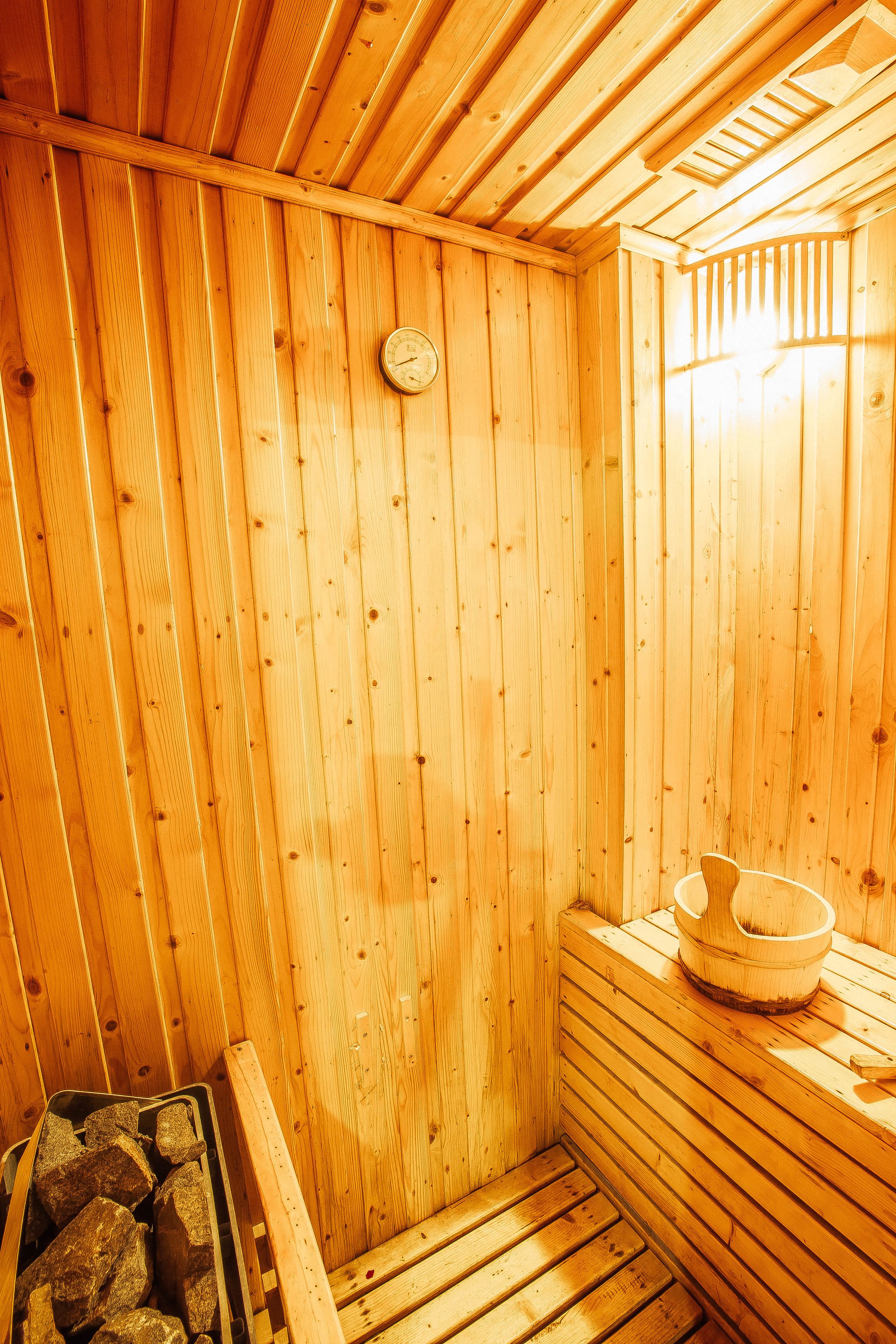 A wooden sauna with a sloped ceiling, a wooden bench, and a wooden basin on the bench.