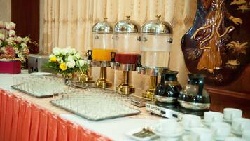 Een buffetopstelling met verschillende drankdispensers, een bloemstuk en een decoratieve vaas.