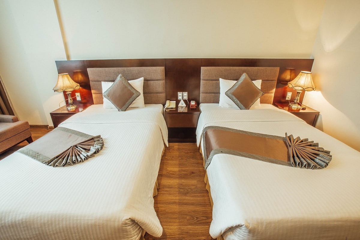 Une chambre d’hôtel avec deux lits, des têtes de lit en bois, des lampes de chevet et une petite table placée entre les lits.