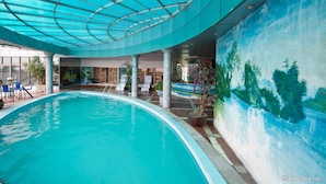 Ein Innenpool mit Glasdecke, Wandgemälde und mehreren Liegestühlen.