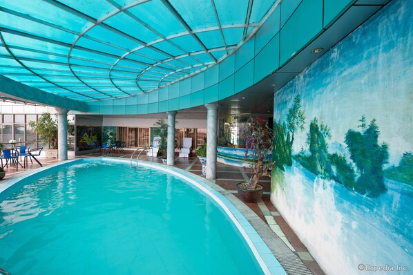 Una piscina interior con techo de vidrio, un mural en la pared y varias sillas de descanso.