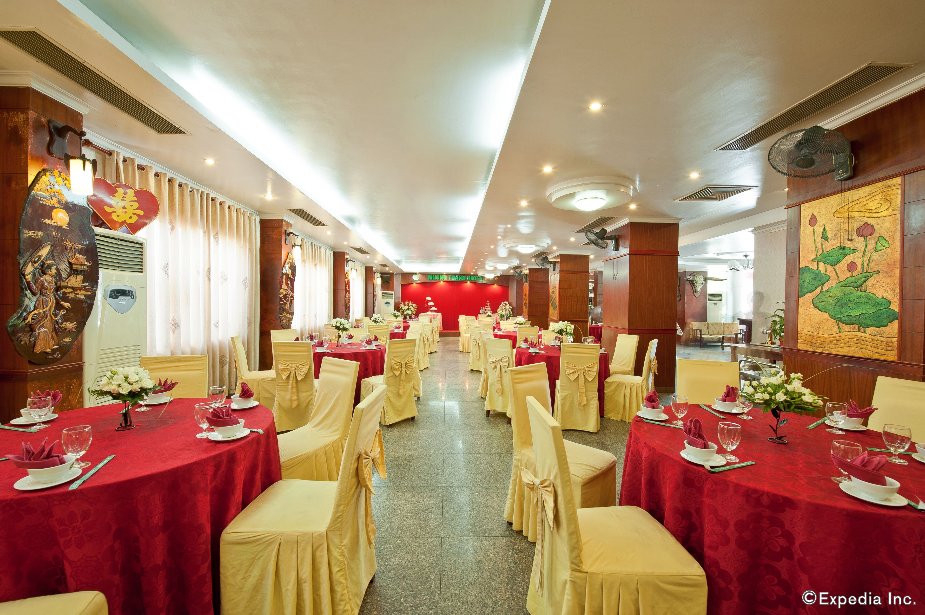 A banquet hall with round tables set for a formal event, featuring red tablecloths and gold chair covers.