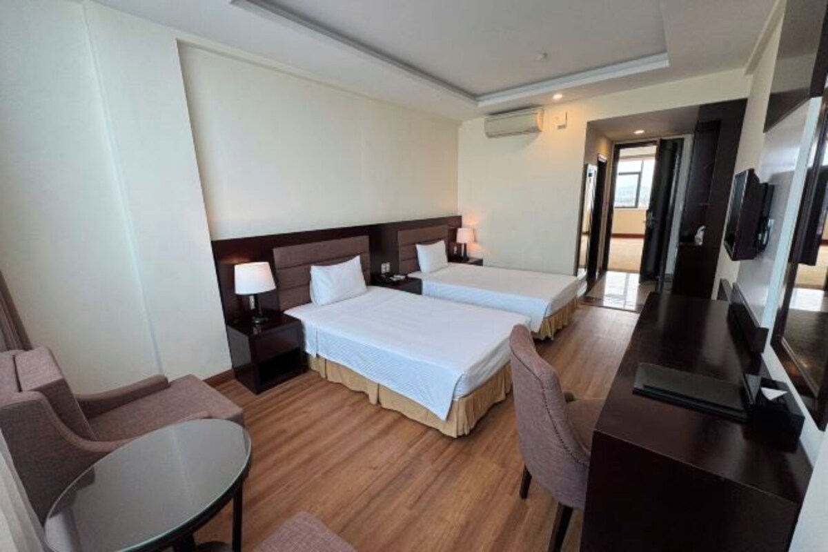 Une chambre d’hôtel avec deux lits, un bureau, une chaise, une petite table et un téléviseur.