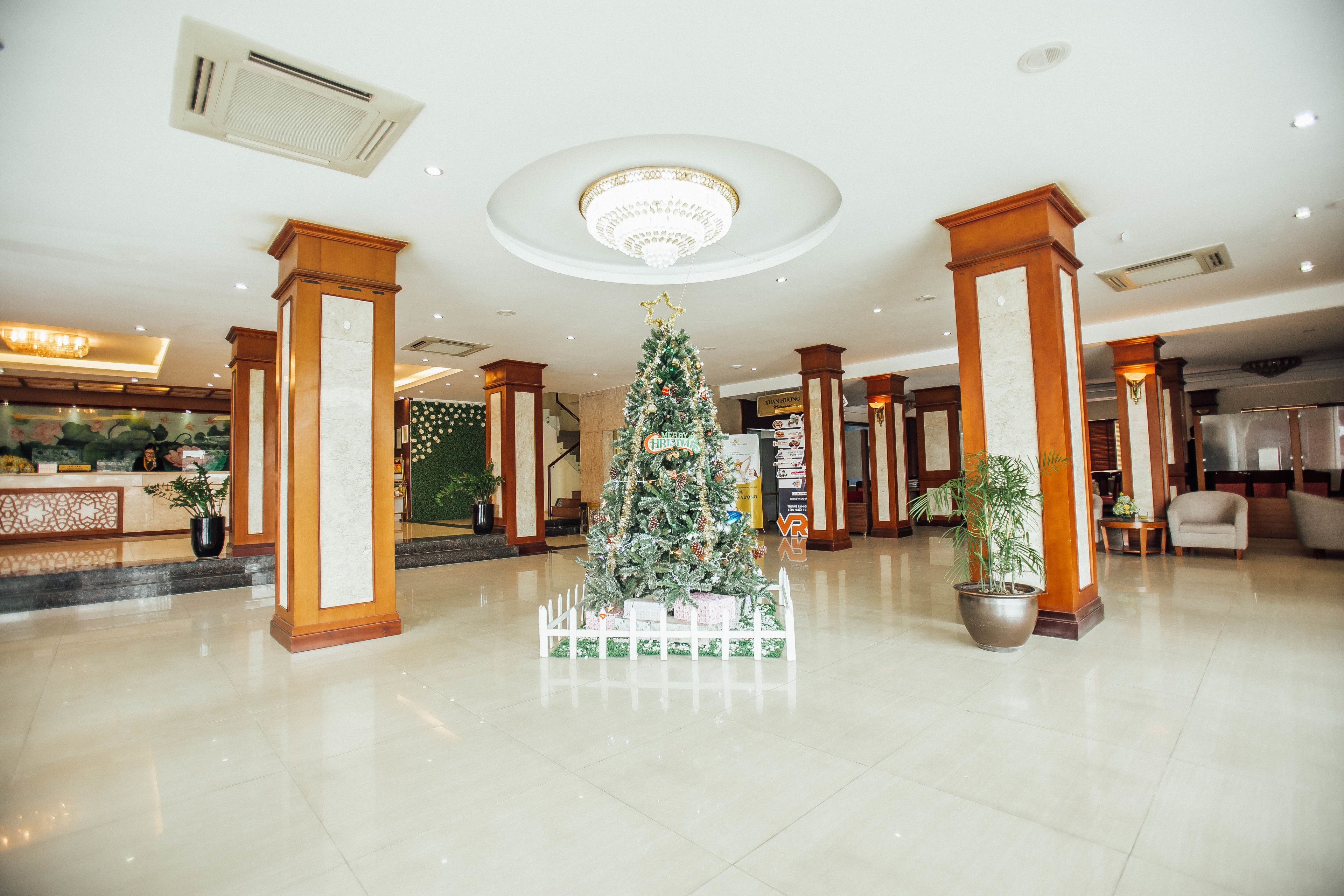 A spacious lobby with a central Christmas tree, marble flooring, and classic wooden pillars.
