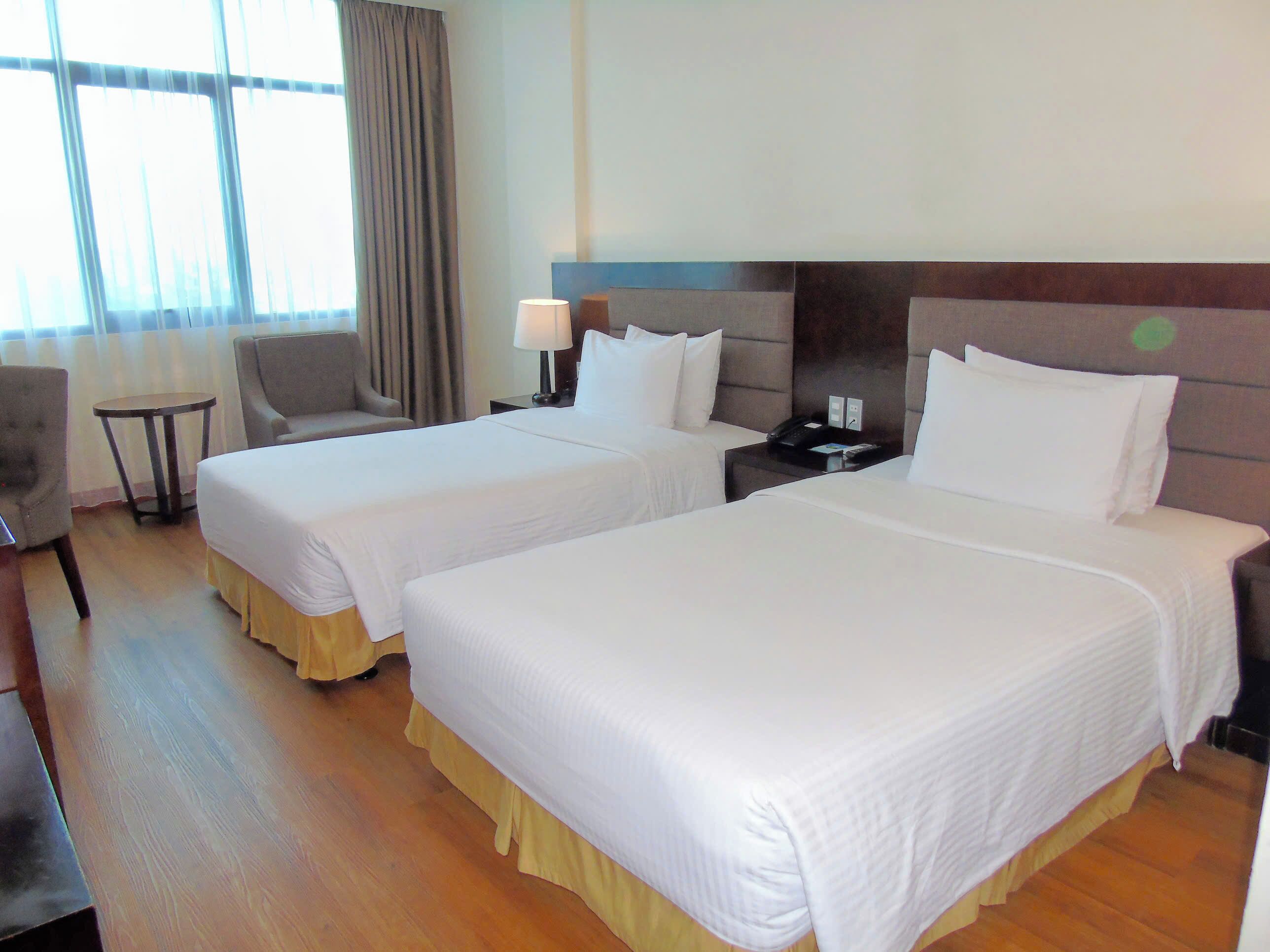 Una habitación de hotel con dos camas, una mesita, una silla y una lámpara.