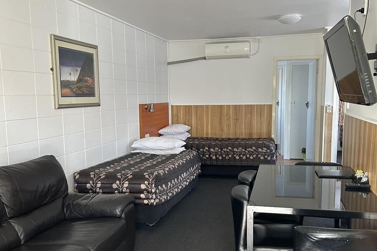 A compact hotel room with a sofa, two single beds, a small table, and a TV.