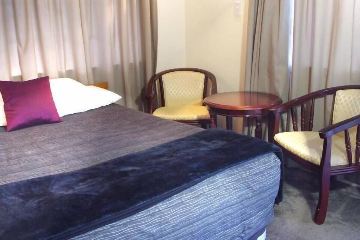 A hotel room with a bed, two chairs, a small table, and curtains.