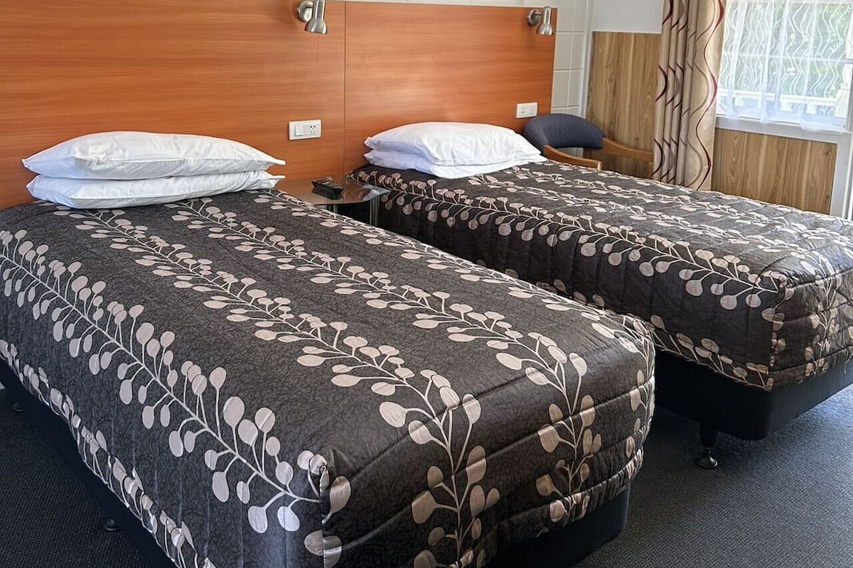 A hotel room with two beds, a wooden headboard, a painting on the wall, and a window with curtains.