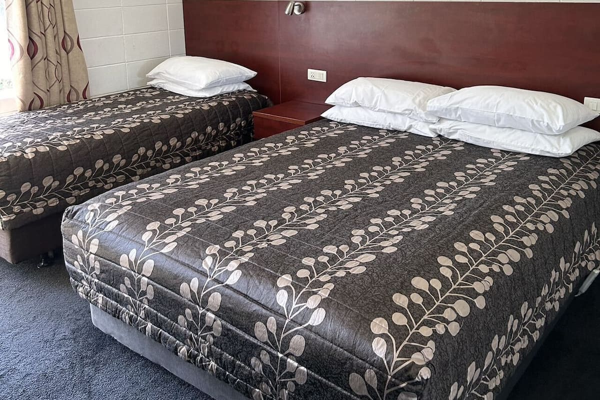 A hotel room with a large bed, two bedside tables, a headboard, and a curtain.