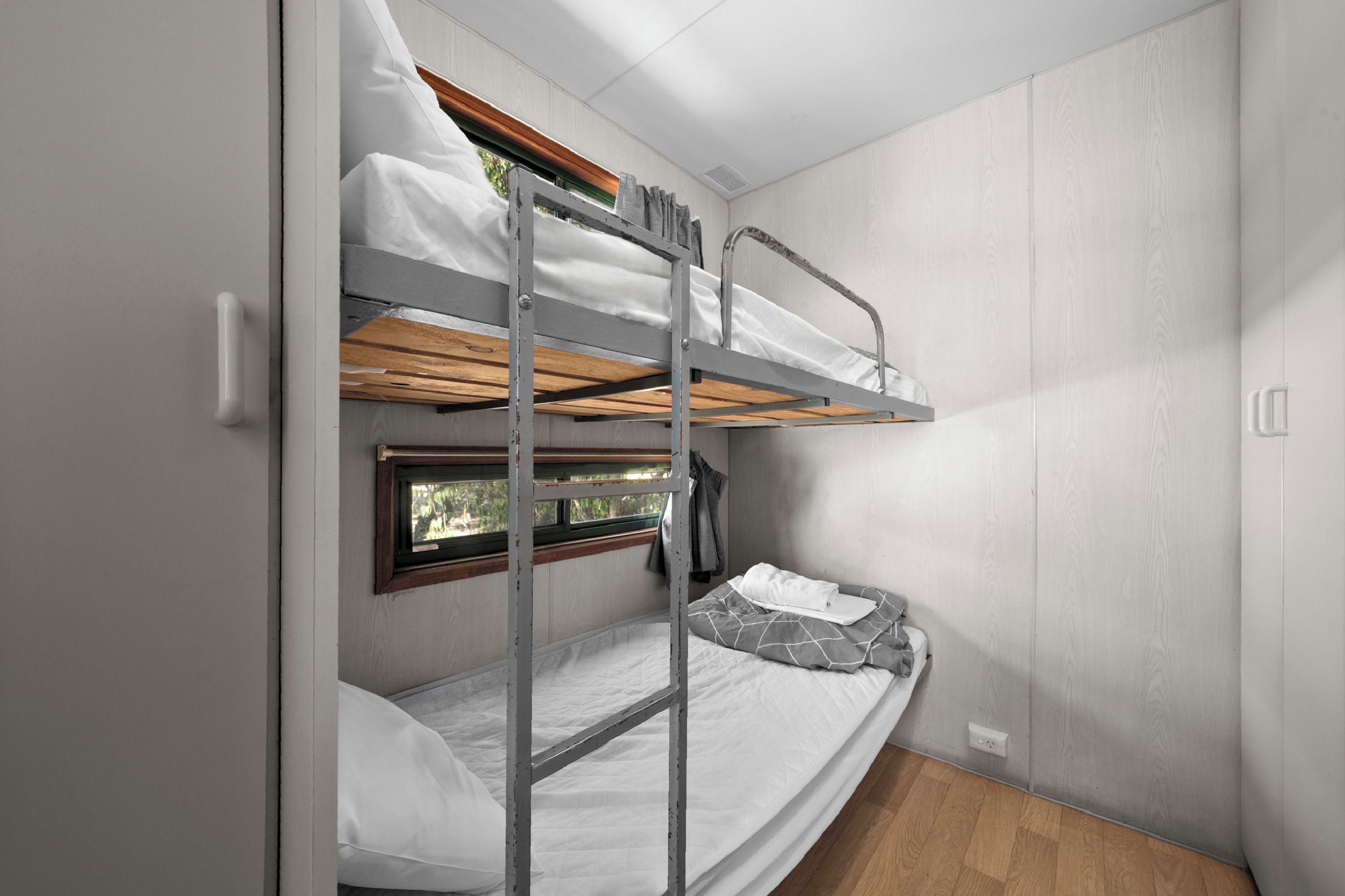 A bunk bed with a window, a small bedside table, and a power outlet.
