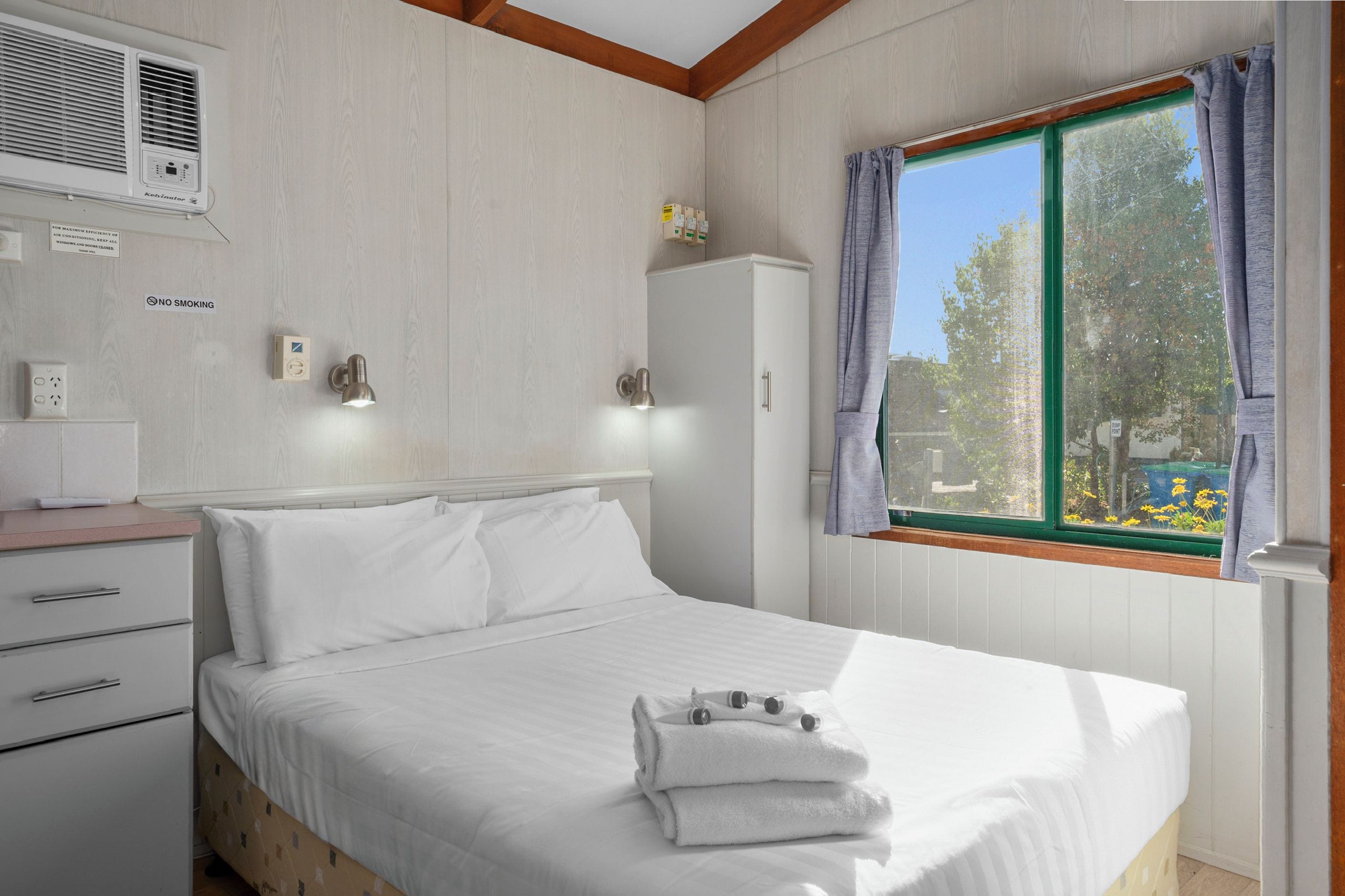 Un dormitorio con cama, armario, ventana con cortinas y aire acondicionado de pared.