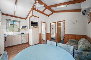 Une pièce compacte et bien éclairée, comprenant un coin cuisine, un lit et un espace salon.