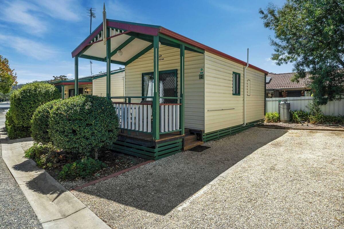 Une petite maison mobile d’un seul étage, dotée d’un porche couvert et d’un petit jardin à l’avant.