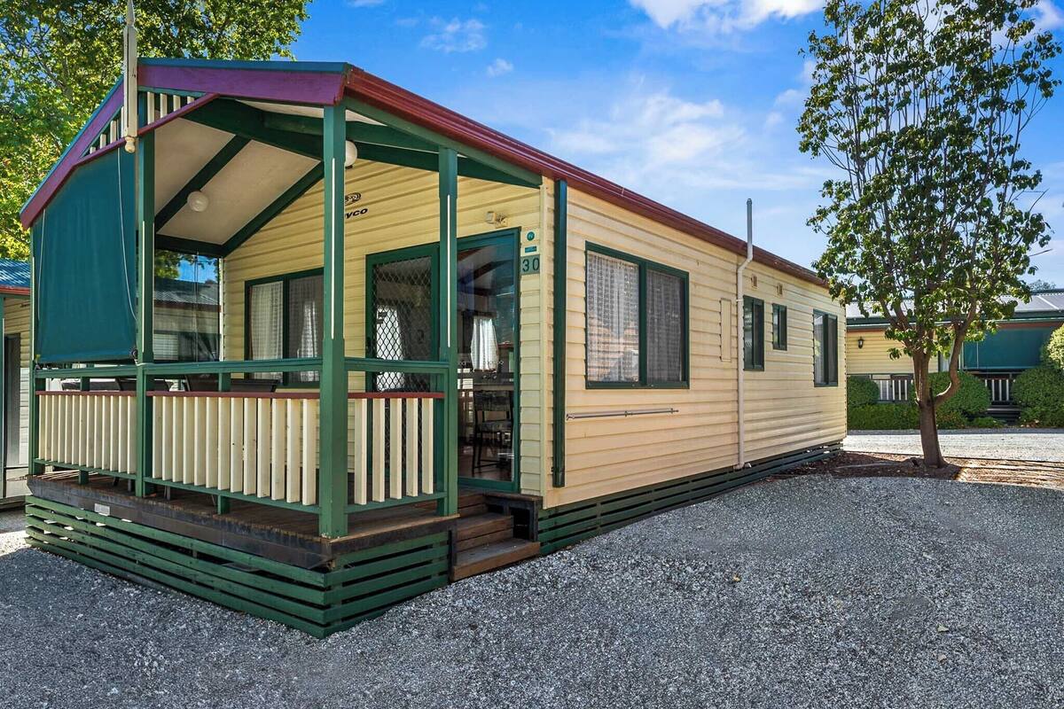 Une maison mobile avec une véranda, une fenêtre avec un rideau et le numéro « 30 » sur la porte.