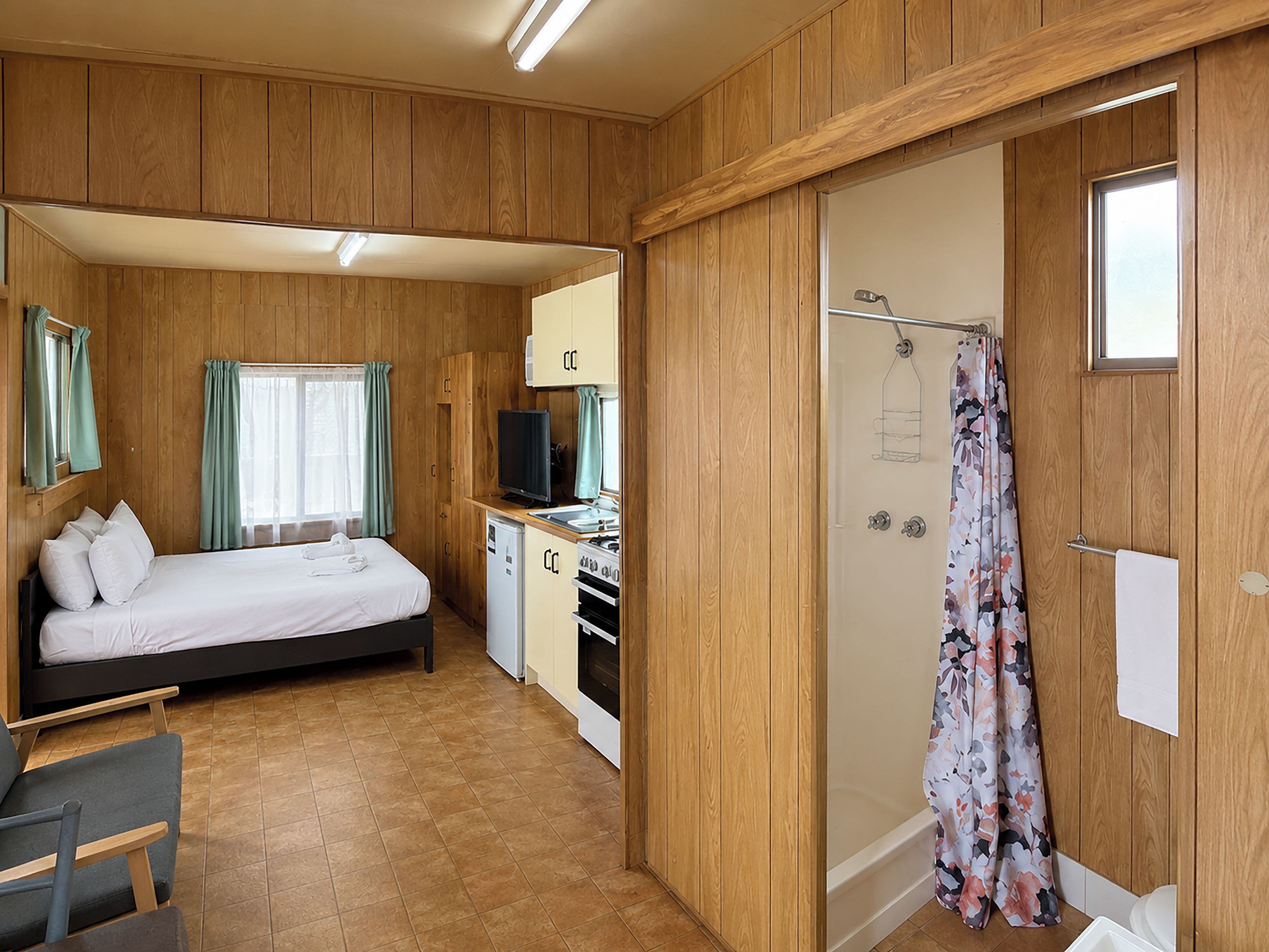 Habitación compacta con cama, kitchenette pequeño, ducha y ventana con cortinas.