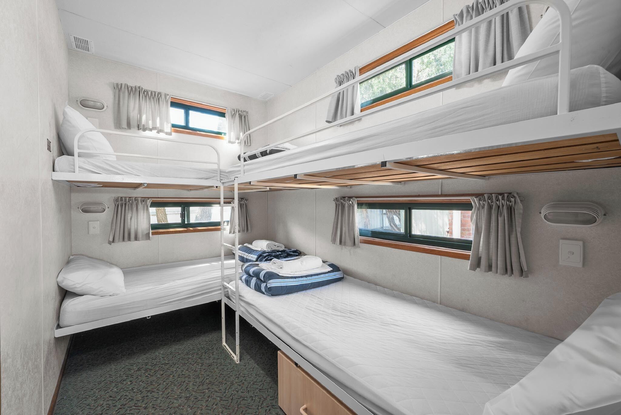 A compact, well-lit room with bunk beds, a small window with curtains, and a built-in heater.