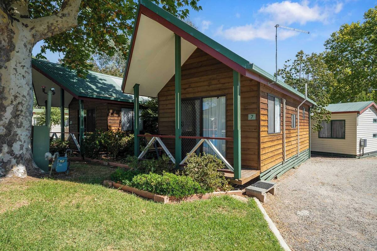 Une cabane en bois avec un toit vert, une véranda et un petit jardin.