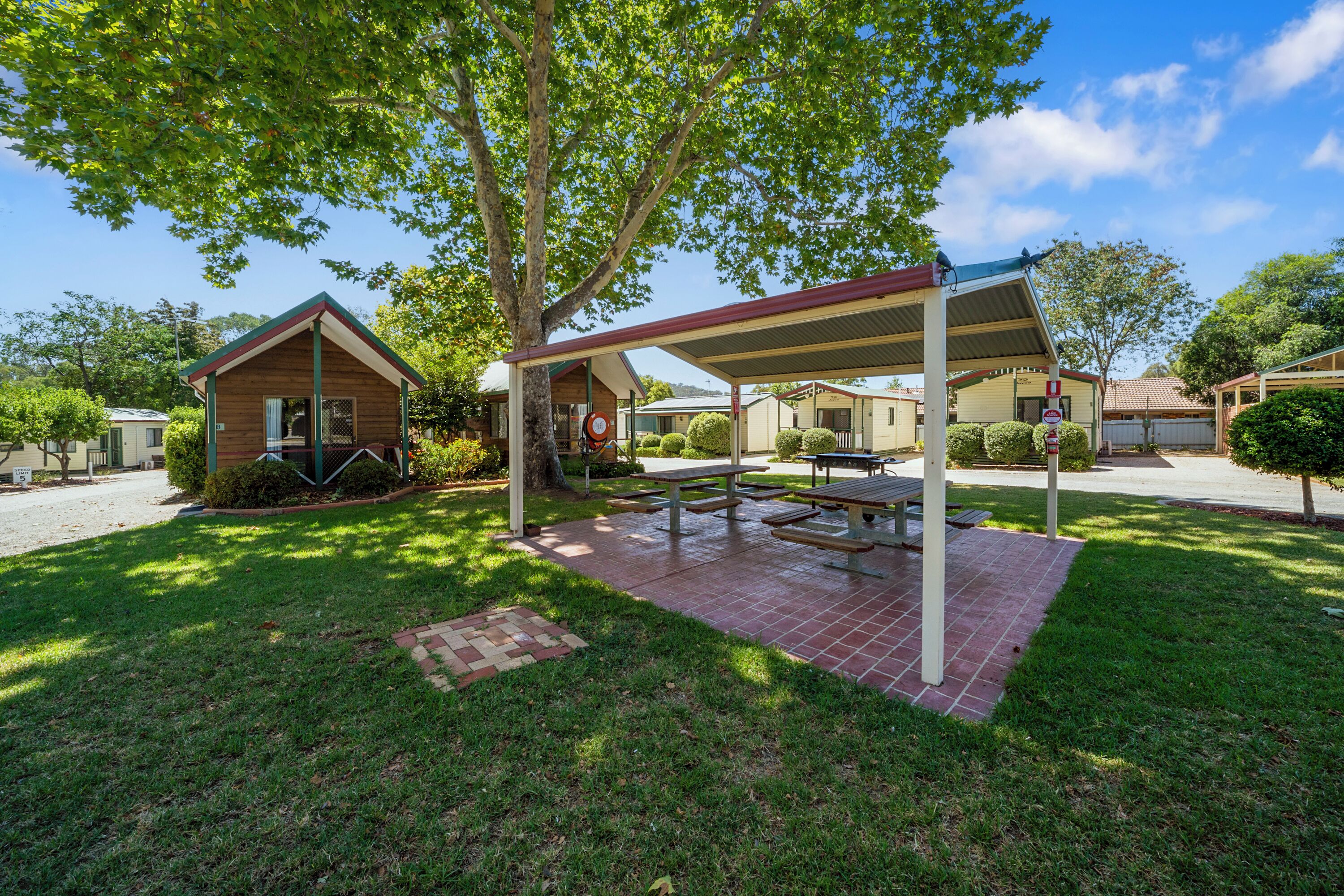 Un área de picnic techada con mesas, un pequeño edificio y un árbol que da sombra.