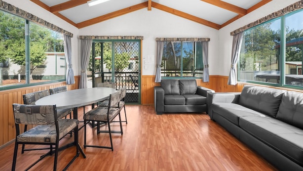 Una habitación amplia con suelo de madera, una gran mesa de comedor con sillas, un sofá y un ventilador de techo.
