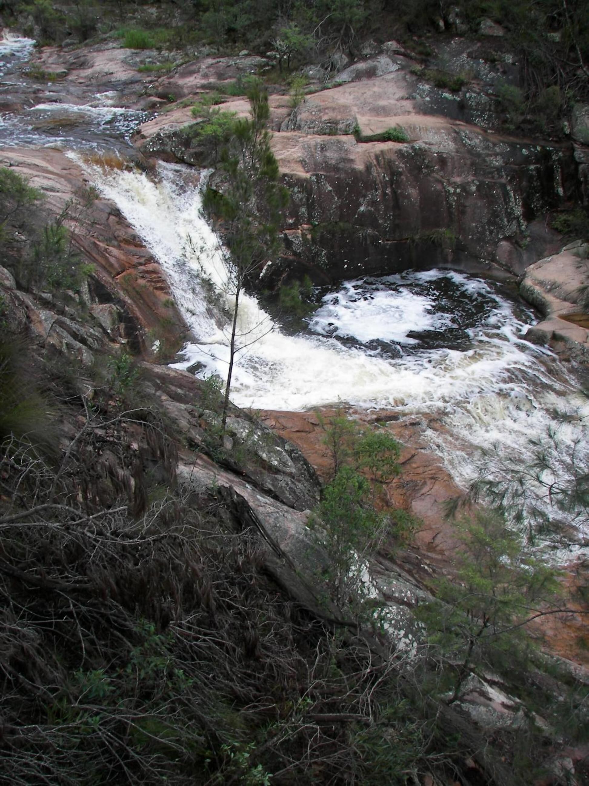 Una cascada natural rodeada de terreno rocoso y vegetación escasa.