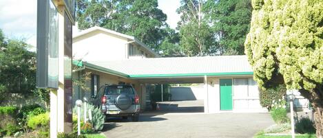 A building with a covered parking area and a car parked in front.