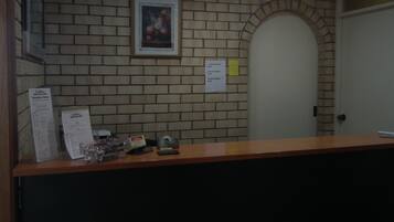 Zona de recepción con pared de ladrillo, una obra de arte enmarcada, una puerta y un mostrador con un menú y un teléfono.