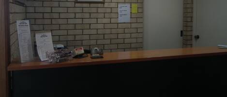 Zona de recepción con pared de ladrillo, una obra de arte enmarcada, una puerta y un mostrador con un menú y un teléfono.