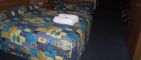 Habitación de hotel con dos camas, una pared de ladrillo, un cuadro pequeño y un escritorio.