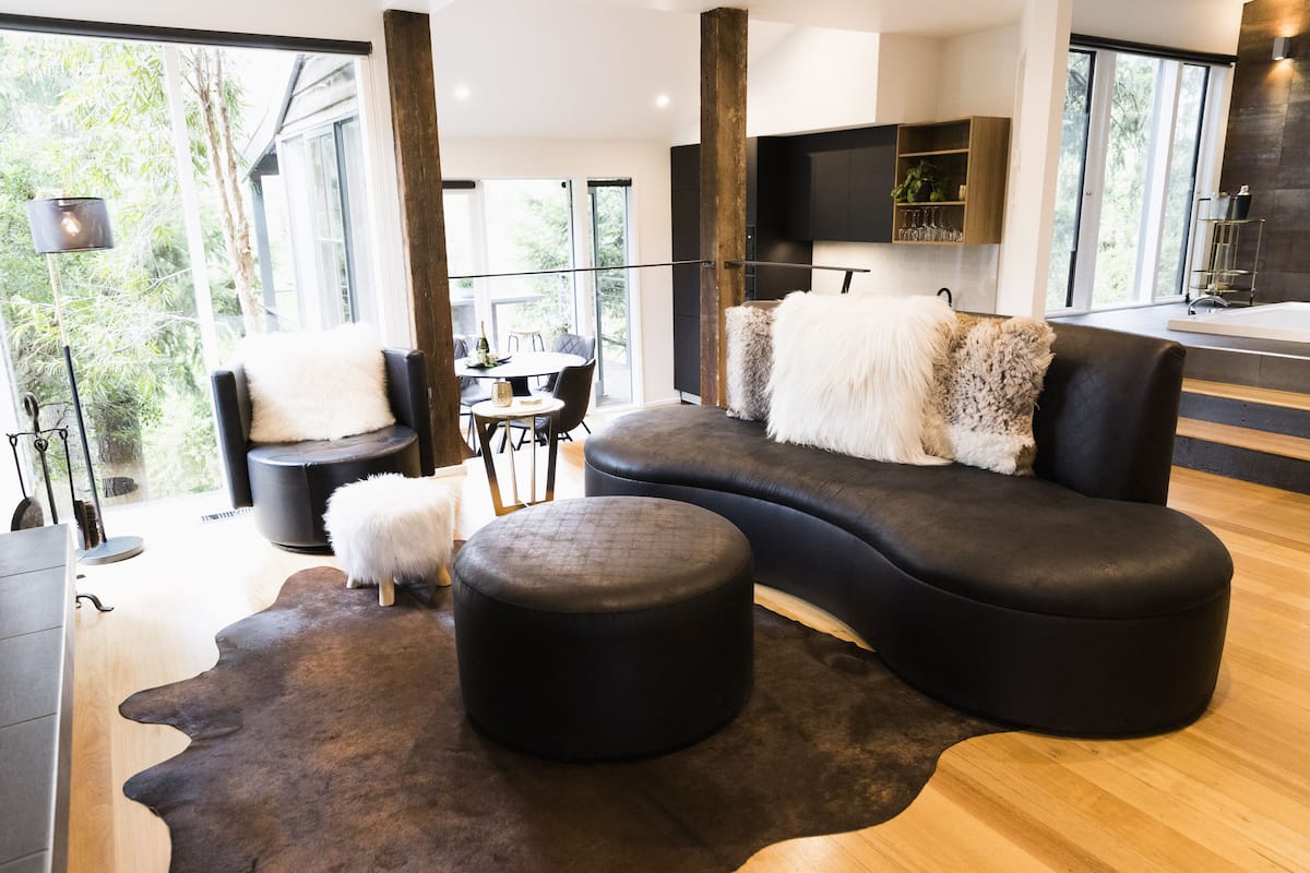 A modern living room with a curved black sofa, a round ottoman, and a dining area with a table and chairs.