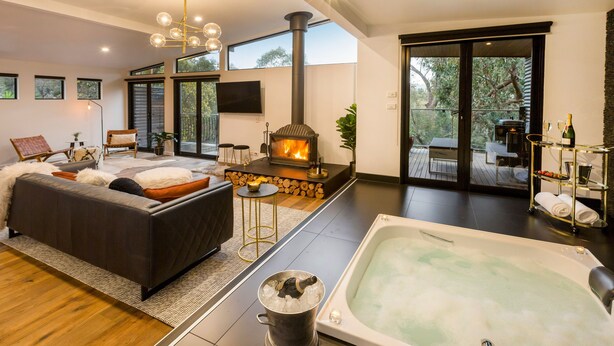 Una sala de estar moderna con chimenea, una bañera grande y un balcón con mobiliario exterior.