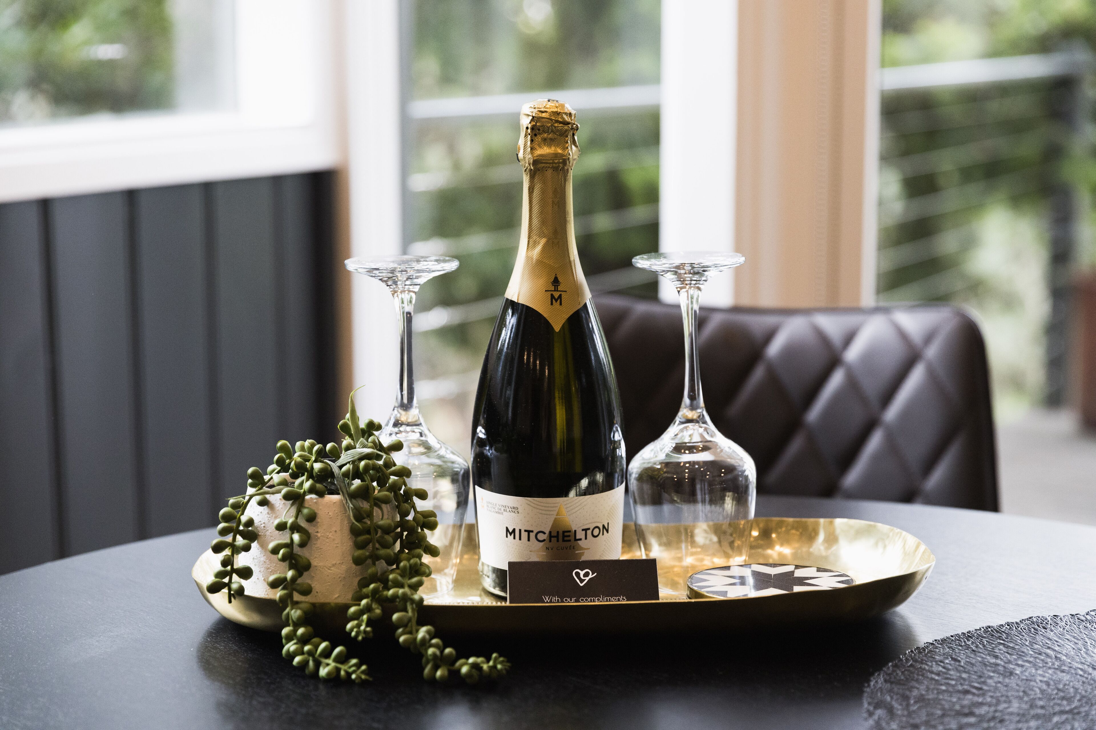 A bottle of Mitchelton champagne on a tray with two glasses and a decorative plant.